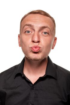 Handsome young blond man in a black shirt is making faces and act like kissing someone, isolated on a white background