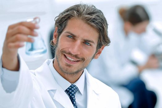 Concentrated male laboratory scientist holding flask with blue liquid showing it to student at science lab.