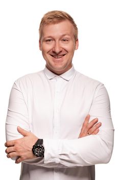 Imposing, young, blond man in a white shirt, with crossed hands and black watches is smiling, while standing isolated on a white background