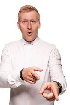 Imposing, young, blond man in a white shirt, with black watches is pointing on something and looking wondered, while standing isolated on a white background