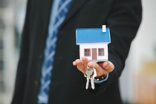 Businessman holding a house model and House Keys.