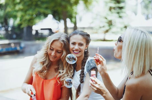 Three girlfriends blowing bubbles on the city street