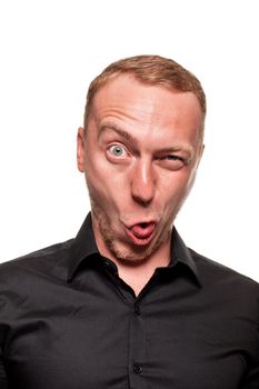 Handsome young blond man in a black shirt is making faces, winks and shows his tongue, isolated on a white background