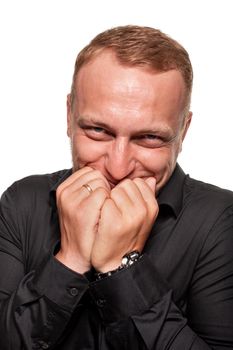 Handsome young blond man in a black shirt makes faces, smiles and closes his mouth with his arms, isolated on a white background