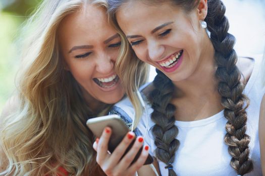 Two girlfriends outdoors having fun with smartphone
