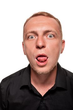 Handsome young blond man in a black shirt is making faces and showing his tongue, isolated on a white background