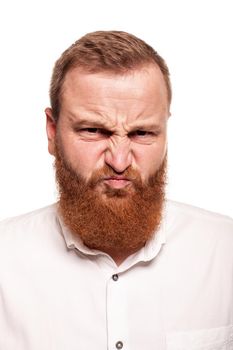 Portrait of a young, chubby, redheaded man in a white shirt making faces and twisted at the camera, isolated on a white background