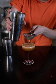 Barman is making cocktail at night club. stylish young man mixing a cocktail in a dark loft cafe. alcohol drink in modern bar. male bartender.