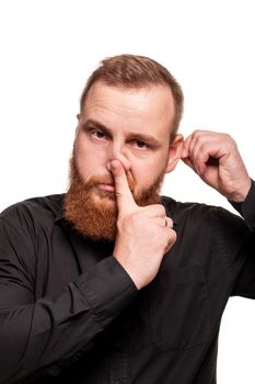 Portrait of a young, chubby, redheaded man with a beard in a black shirt, touching his nose and ear, isolated on a white background