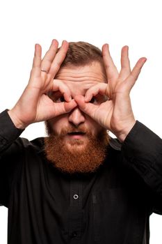 Portrait of a young, chubby, redheaded man with a beard in a black shirt, makes faces at the camera, isolated on a white background