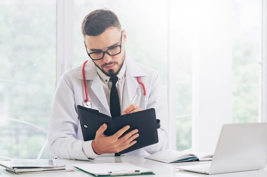 Doctor reading while writing note on a book at office in the hospital. Medical and healthcare concept.