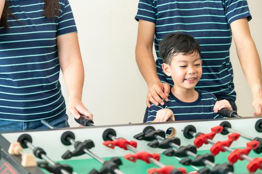 Happy kid playing foosball table soccer with family, father and mother.