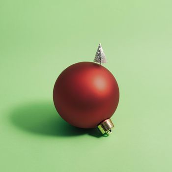 Christmas ball decorated with a Christmas tree against green background. Minimal concept. Square.