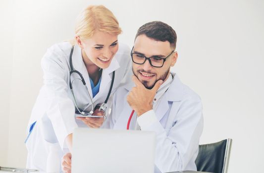 Doctor at hospital office working on laptop computer on the table with another doctor having discussion about patients health.