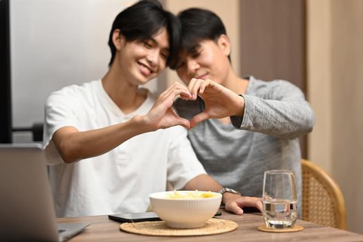 Young homosexual couple making heart with their hands. LGBT, pride, relationships and equality concept.