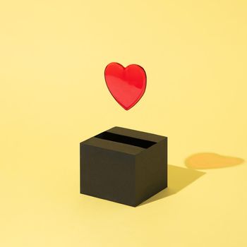 Red heart comes out of a black box and floats on a yellow background. Valentine's Day. Abstract. Square layout with copy space.