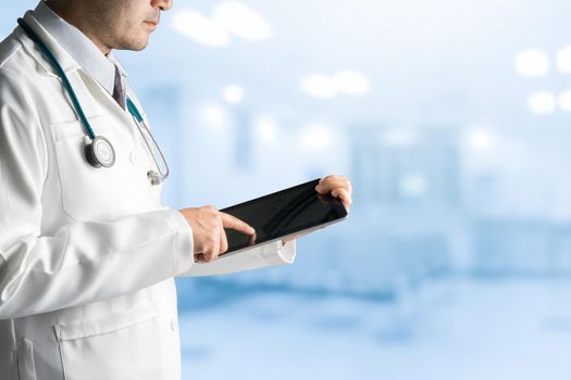 Male doctor using tablet computer to analyze patient health data record, standing on hospital background. Medical technology concept.