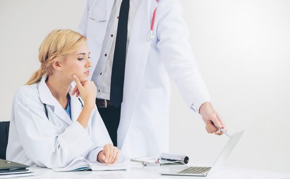 Doctor at hospital office working on laptop computer on the table with another doctor having discussion about patients health.