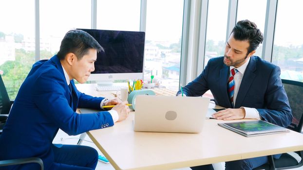 Two business people talk project strategy at office meeting room. Businessman discuss project planning with colleague at modern workplace while having conversation and advice on financial data report.