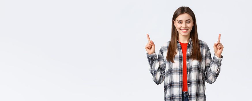 Lifestyle, different emotions, leisure activities concept. Confident smiling girl in checked shirt, turn attention to upper banner, pointing fingers up and look camera, telling about advertisement.