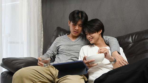 Loving same sex male couple embracing and surfing internet with digital tablet together. LGBT, pride, relationships and equality concept.