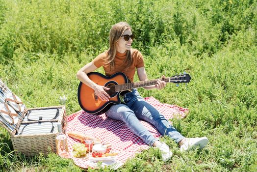 millennial woman in summer clothes and sunglasses playing guitar on a picnic