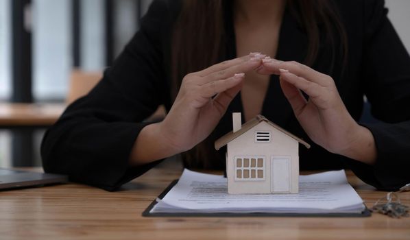 Property insurance and security concept. Protecting gesture of man and symbol of the house. Wide banner composition with office in background..