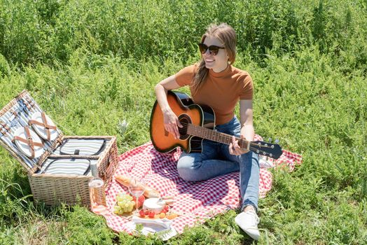 millennial woman in summer clothes and sunglasses playing guitar on a picnic