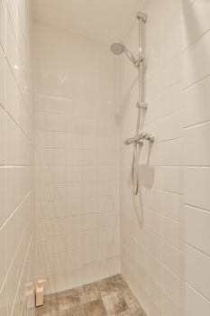 Shower faucets attached to tiled wall near glass partition and ornamental curtail in washroom at home