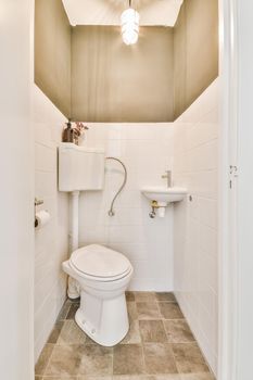 Modern flush toilet and ceramic sink installed on white tiled walls near mirror and towel in small restroom at home