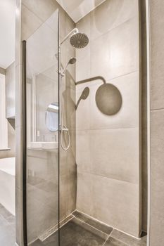 Shower faucets attached to tiled wall near glass partition and ornamental curtail in washroom at home