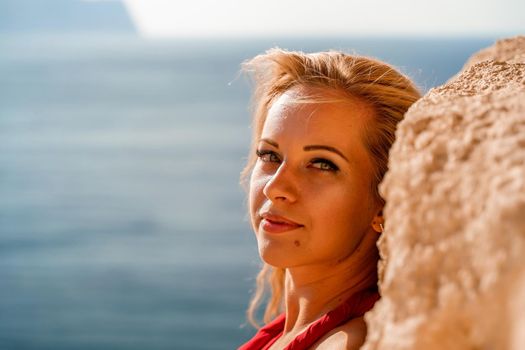 Smiling young woman in a red dress looks at the camera. A beautiful tanned girl enjoys her summer holidays at the sea. Portrait of a stylish carefree woman laughing at the ocean