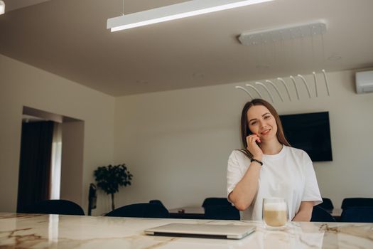 Talks by the phone. Young european woman is indoors at kitchen indoors with healthy food