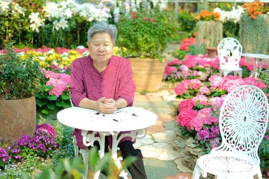 old elder woman resting in flower garden. asian elderly female relaxing in park. senior leisure lifestyle