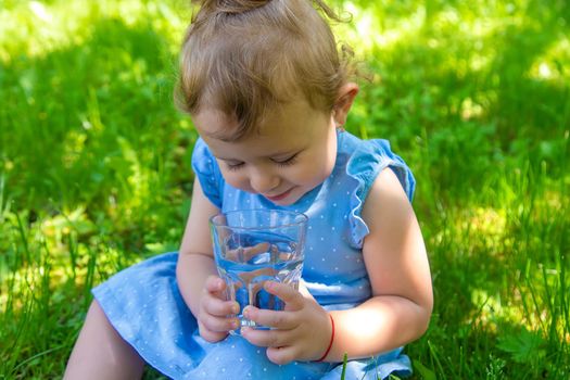 The child drinks water from a glass. Selective focus. Kid.