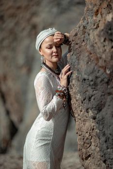 Middle aged woman looks good with blond hair, boho style in white long dress on the beach decorations on her neck and arms