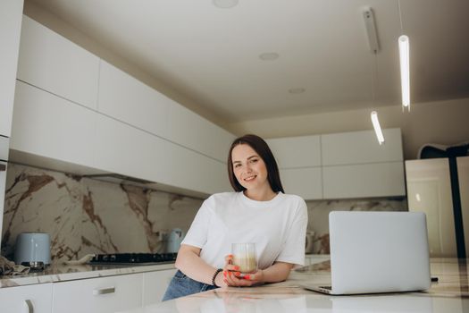 Focused young woman sitting at her kitchen table at home working on her small business with a laptop.