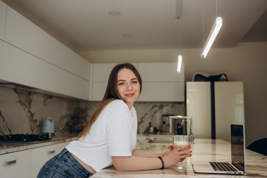Attractive young woman working on laptop while sitting in the kitchen at home