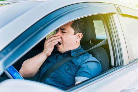 A sleepy driver at the wheel, a tired person while driving, Tired driver yawning, concept of man yawning while driving