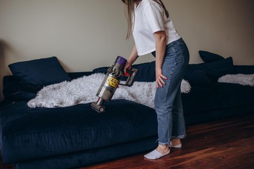 Woman cleaning sofa with a modern cordless vacuum cleaner with a special nozzle, close-up. Dry cleaning concept with wireless vacuum cleaner