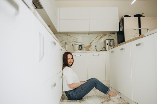 Young woman drinking coffee on floor in kitchen.