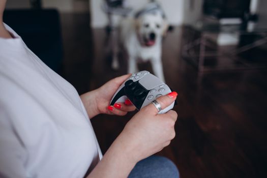 A young woman is playing a game console. Girl gamer and computer video games. The streamer holds a joystick in her hands. Person at home at night. Labrador dog on the background