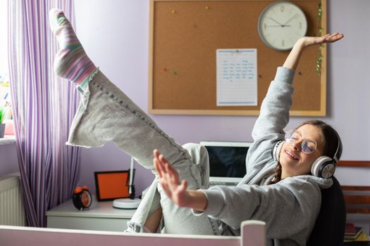 A young girl puts her arms and legs up while listening to music. Smiling and happy, the brunette girl is waving her legs.
