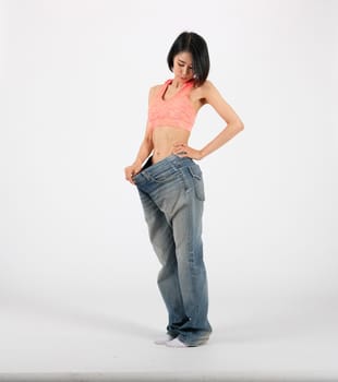 sporty fitness woman in loose jeans after losing weight on white background. healthy sport lifestyle