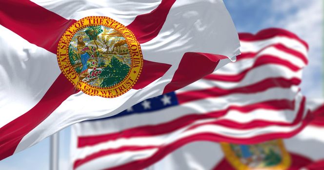 The Florida state flag waving along with the national flag of the United States of America. In the background there is a clear sky.