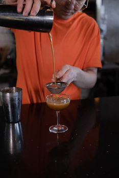 Barman is making cocktail at night club. stylish young man mixing a cocktail in a dark loft cafe. alcohol drink in modern bar. male bartender.