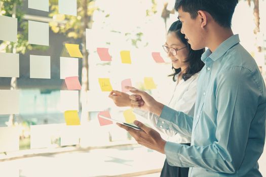 business people working planning discussing idea with sticky reminder note on glass wall at workplace