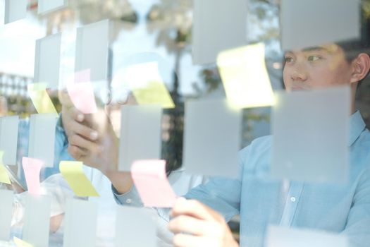 business people working planning discussing idea with sticky reminder note on glass wall at workplace