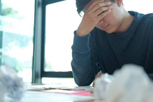 man feeling tired, frustrated & stressed from hard work with crumpled crushed paper on desk. exhausted freelancer have headache at workplace.