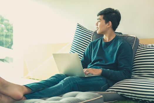 man sitting on floor in living room using computer at home. male teenager student studying doing assignment